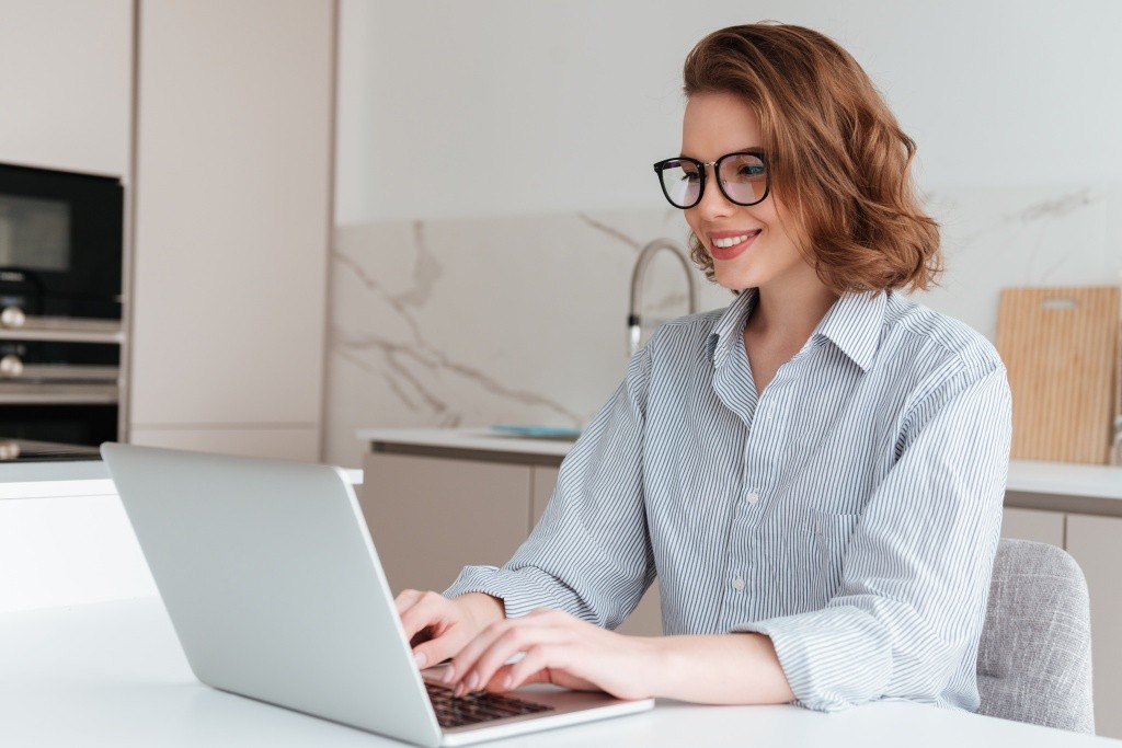 elegant-smiling-woman-in-glasses-and-striped-shirt-using-laptop-computer-while-siting-at-table-in-kitchen.jpg